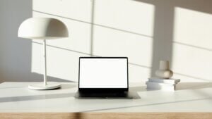 Minimalist desk setup featuring a laptop, stylish lamp, and books in natural light.